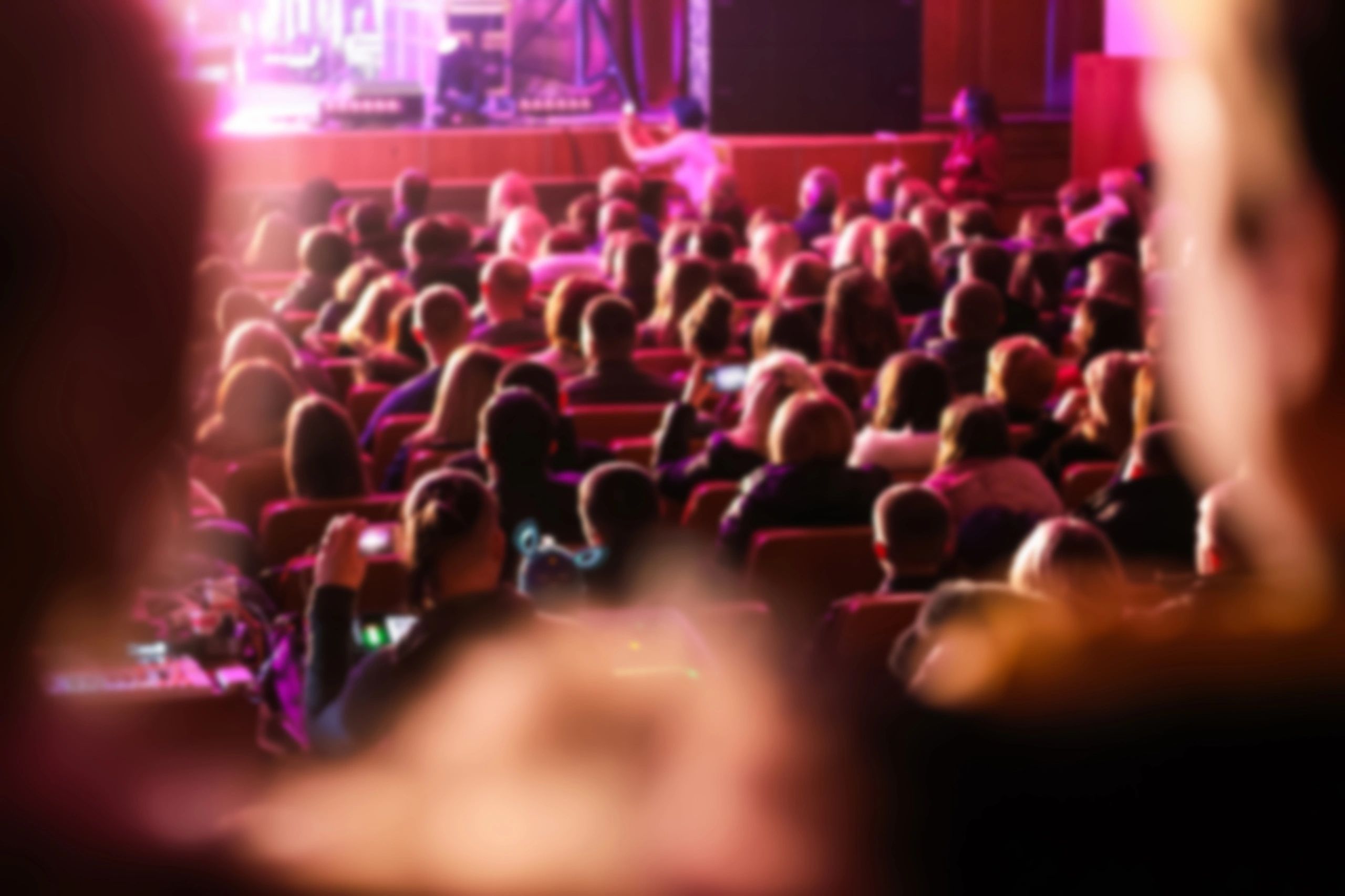 Audience seated in a theater with stage out of focus